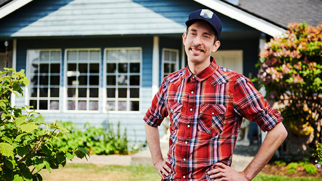 a man in a hat and plaid shirt standing in front of a house