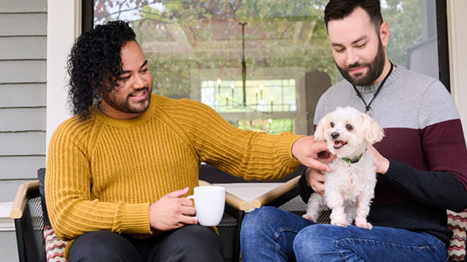 two men sitting on a chair petting a dog