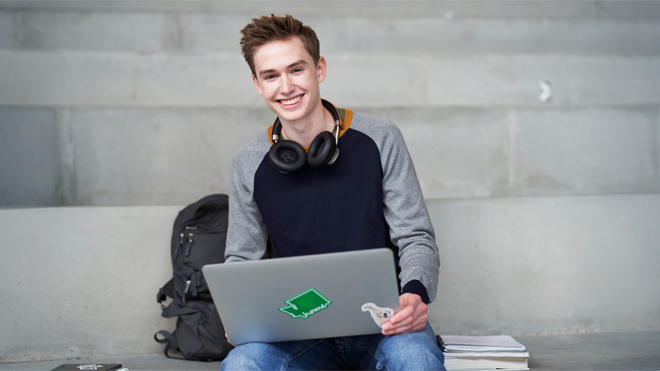 A smiling student with his headphones, laptop, and backpack.