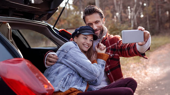 A woman and man taking a selfie while sitting in the back of their vehicle.