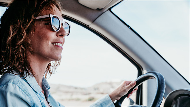 A smiling woman wearing sunglasses driving a vehicle.