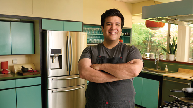 Man standing in kitchen with his arms crossed and smiling
