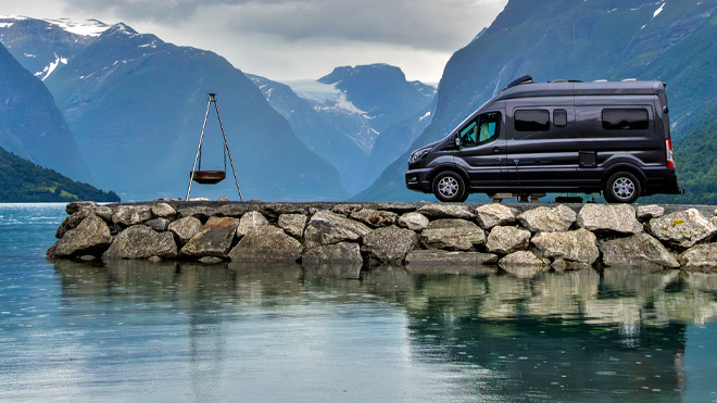 A black RV near a lake with mountains in the background