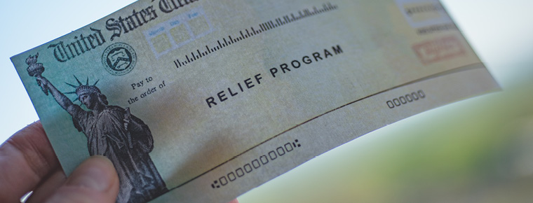 A hand holding a check labeled "relief program" from the United States government 