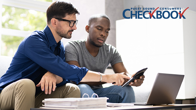 Two men sitting close together on a gray couch. The man on the left is wearing a blue shirt and glasses and is pointing at a tablet in other man's hand. Man on right is wearing a gray shirt. Consumers' Checkbook logo in upper right corner.