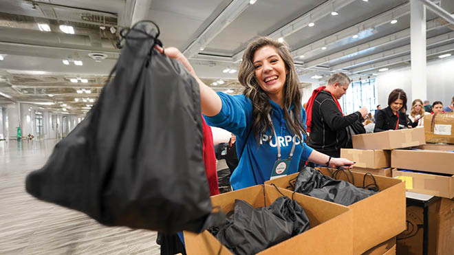 A woman stands in a warehouse, holding a bag filled with clothes, ready to sort or donate the items inside.