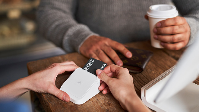 This image is a close up of someone paying for a transaction with a BECU visa credit card. One person's hands are on their wallet, and the other persons hands are inserting the credit card into a wireless point of sale card reader. They are at what appears to be a wood countertop. 
