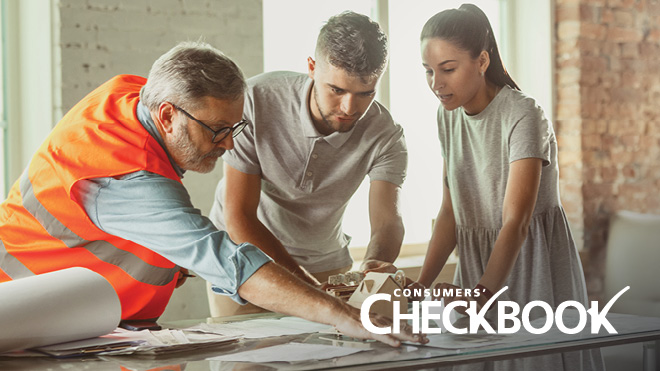 This is an image of three people looking at paperwork on a desk. The setting of the photo suggests a couple is getting a consultation with a home contractor. The contractor is on the left side of the image and is wearing a bright orange vest. He's wearing glasses and is pointing at paperwork on a table. In the middle is a man, who is wearing a gray shirt. Both of his hands are resting on the table, as he looks down at the paperwork. On the right-hand side is a woman. She is also wearing a gray shirt and has a ponytail. Both her hands are also resting on the table, as she looks down at the paperwork. In the background is a window and brick walls. 