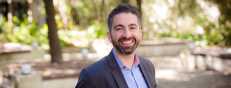A headshot of BECU employee Nadim Homsany. He's posed outside and is wearing a dark blazer and checkered shirt.