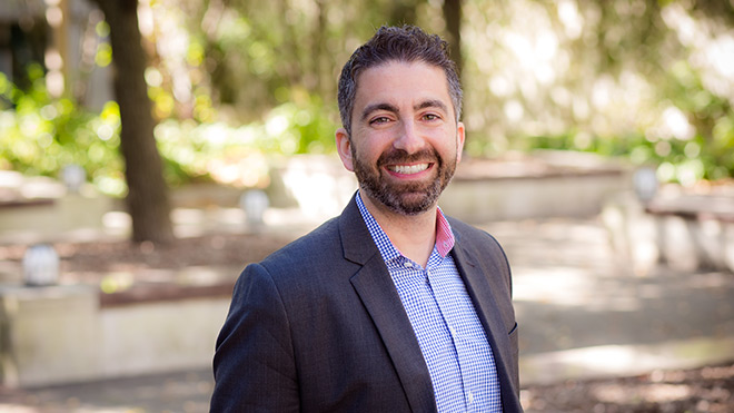 A headshot of BECU employee Nadim Homsany. He's posed outside and is wearing a dark blazer and checkered shirt.