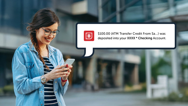 A woman smiles while looking down at her phone. To the right is a pop-up illustration of a BECU banking alert. The notification says, " $100.00 (ATM Transfer Credit From Sa...) was deposited into your XXXX * Checking Account." 
