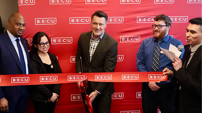 A group of BECU employees and supporters smiling as they cut a ribbon together at a grand opening event.