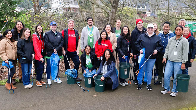 A group of BECU employees on a trail, posing with clean up materials such as buckets, garbage picks and trash bags. 