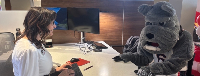 BECU employee sits at a desk inside a Spokane branch of BECU across from Gonzaga mascot Spike the bulldog.