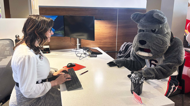 BECU employee sits at a desk inside a Spokane branch of BECU across from Gonzaga mascot Spike the bulldog.