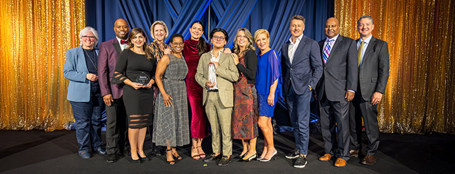 A large group of BECU employees standing on a blue and gold stage during an awards ceremony, with two employees holding awards.