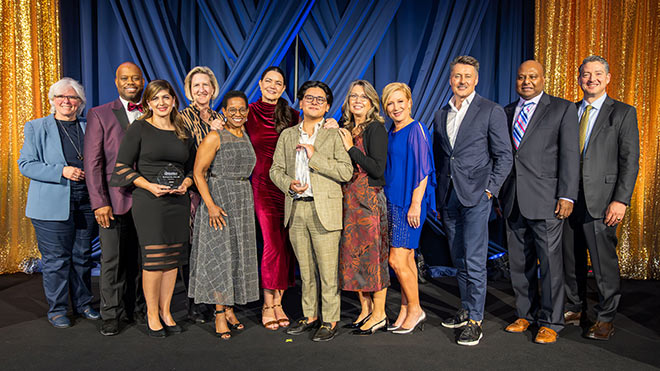 A large group of BECU employees standing on a blue and gold stage during an awards ceremony, with two employees holding awards.