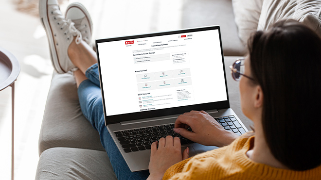 A person sits cross-legged on a couch with their back to the camera. A laptop rests on their lap, displaying a Fraud & Security webpage.