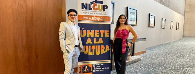 Two people stand beside a “Únete a la cultura” banner for the National Association of Latino Credit Unions & Professionals.
