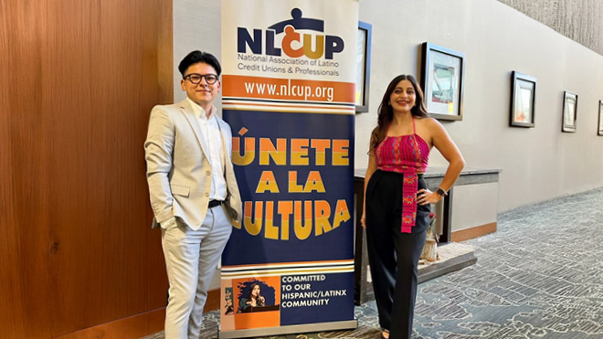 Two people stand beside a “Únete a la cultura” banner for the National Association of Latino Credit Unions & Professionals.