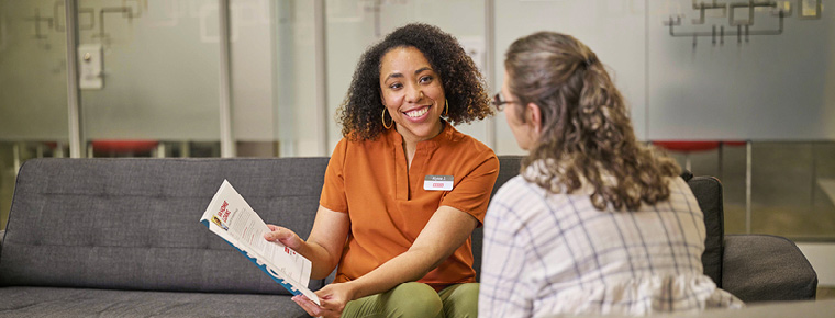 A BECU member consultant shows a brochure to a member. The member consultant is sitting on a couch and smiling at the member who is seated across from her in a cushioned chair facing away from the camera.