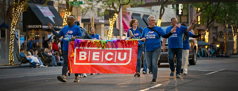 BECU volunteers carry a red BECU banner while walking in a community parade.