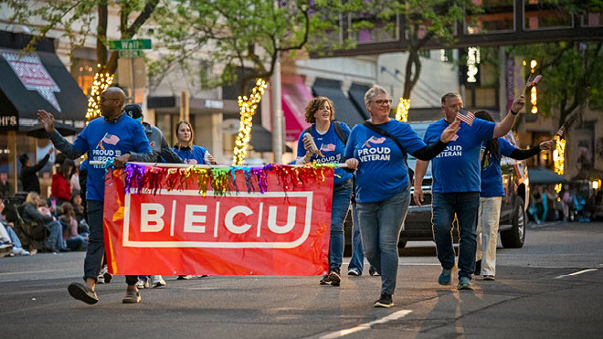 BECU volunteers carry a red BECU banner while walking in a community parade.