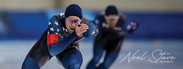 Cooper McLeod speedskating in a blue racing suit, leading a race on an indoor rink.