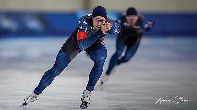 Cooper McLeod speedskating in a blue racing suit, leading a race on an indoor rink.