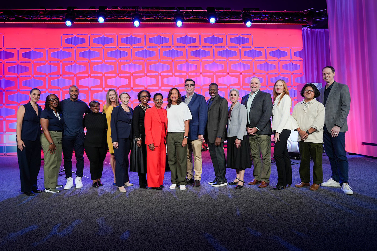 Sixteen people representing BECU, BECU Foundation, BECU Board of Directors and nonprofit partners stand together on a stage with a pink and purple backdrop.