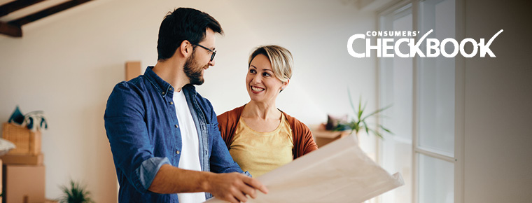 Two people stand together while looking at a large printout of construction plans. The Consumers’ Checkbook logo appears in white in the upper right corner.