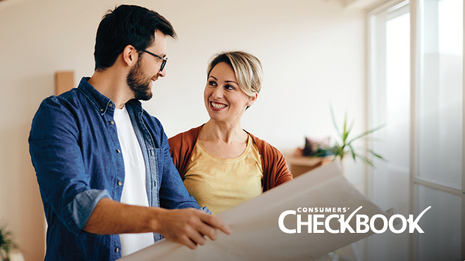 Two people stand together while looking at a large printout of construction plans. The Consumers’ Checkbook logo appears in white in the lower right corner.