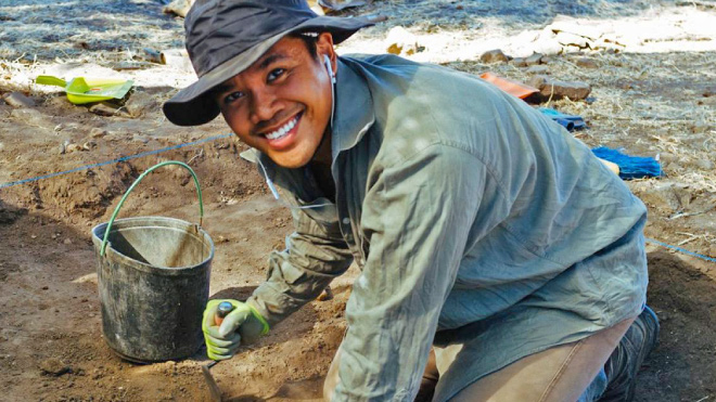 Smiling man wearing a hat digging in sand by the ocean