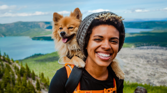 Woman on a hilltop with a dog on her shoulder