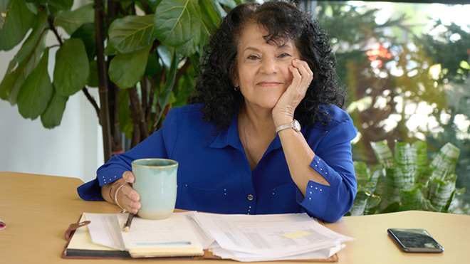 A smiling woman reviewing some documents with a cup of coffee.