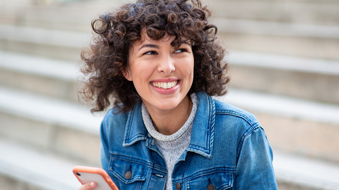 A woman sitting outside on stairs, wearing a blue shirt and holding a phone
