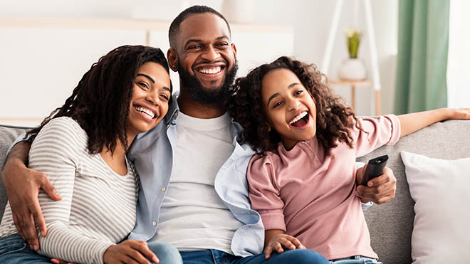 A smiling family while watching something on a tv.