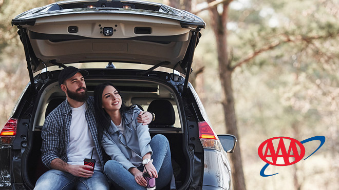 A couple sitting in the open trunk of their vehicle with the AAA logo