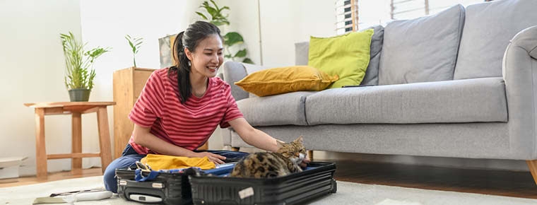 Young person sitting on floor with open suitcase. They are smiling at the cat that settled down in one side of the bag.