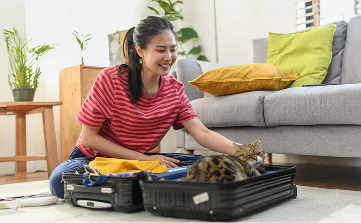 Young person sitting on floor with open suitcase. They are smiling at the cat that settled down in one side of the bag.