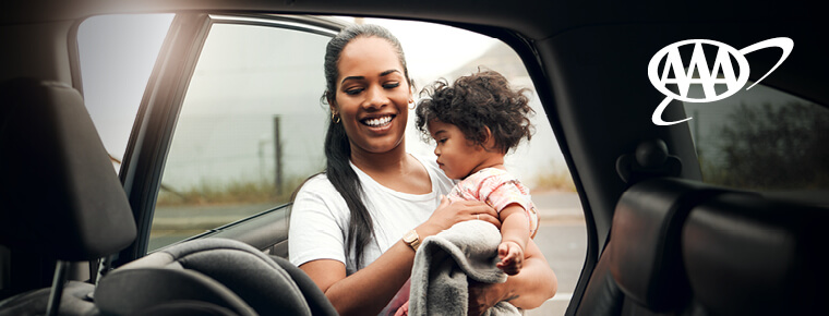 A woman putting her child in a car seat. AAA logo.