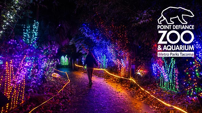 A person walking through the Zoolights displays. Point Defiance Zoo & Aquarium Metro Parks Tacoma logo.