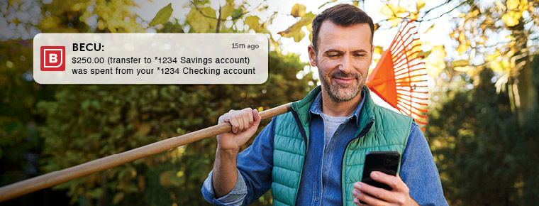 Man holding a rake over his shoulder while looking at the mobile phone in his hand.