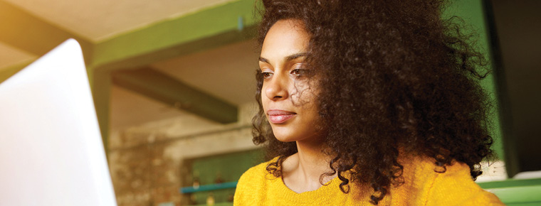 Woman smiling while typing and looking at a laptop screen.