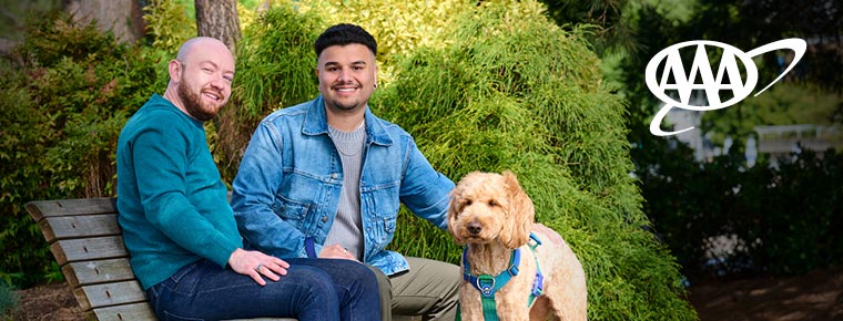 Two smiling men sitting on a park bench while petting a dog