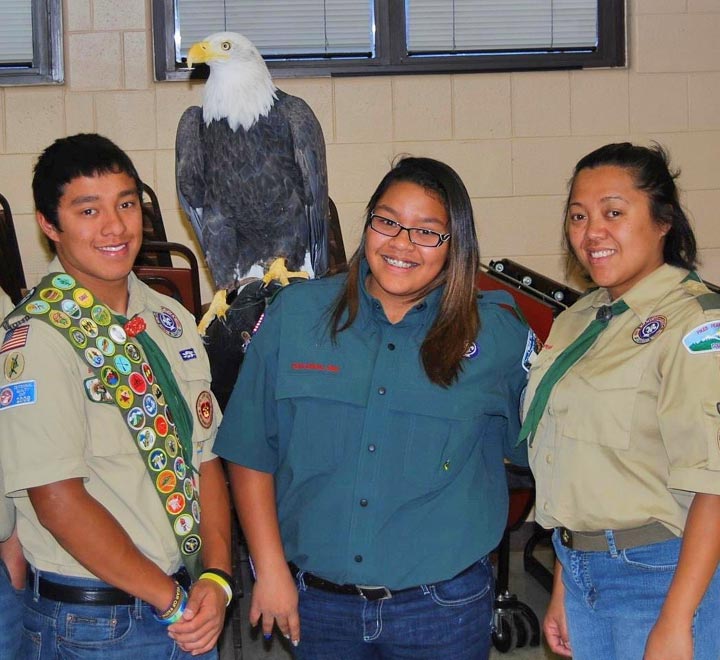 Pauline Hernandez in a scouting shirt and jeans, stands with two scouts. A bald eagle is perched over a scout's shoulder.