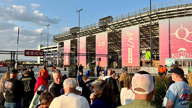 Crowd gathered near an outdoor event entrance with banners reading ‘BECU Live’ and other sponsor logos, next to a stadium.