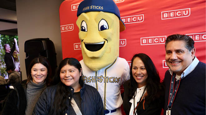 A group of four people pose together with Fin Crispy Jr., West Seattle's DubSea Fish Sticks mascot. 
