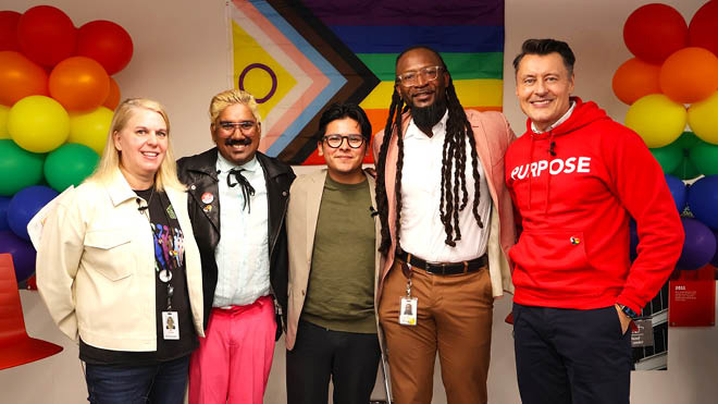 Five BECU employees stand shoulder to shoulder, smiling at the camera. An intersectional Pride flag is behind them with a tower of balloons in rainbow colors on either side.
