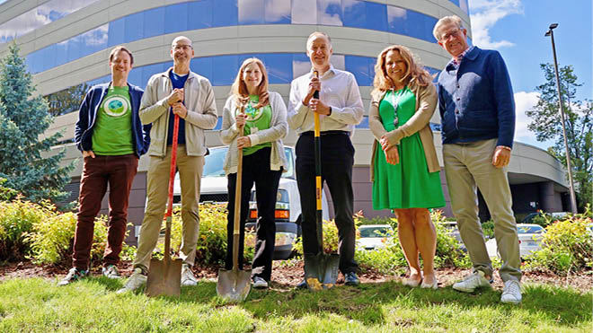 A group of BECU employees holding shovels stands in front of the Tukwila Neighborhood Financial Center, ready for a pollinator garden groundbreaking.